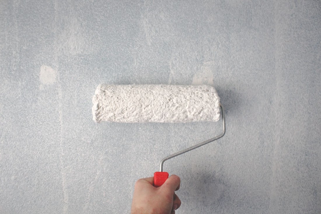 Farbrolle mit weißer Farbe auf einer Wand